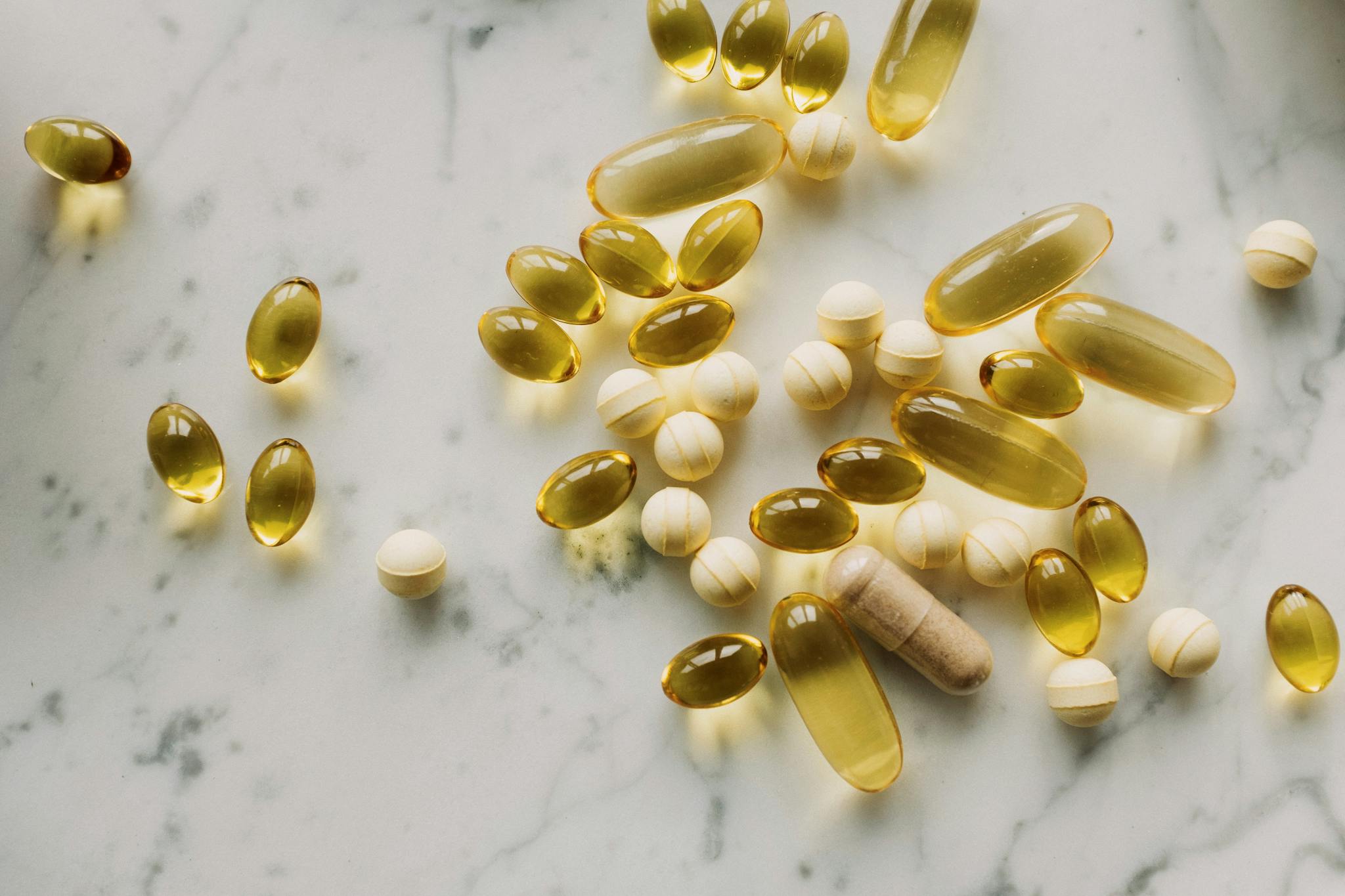 A variety of capsules and pills scattered on a light marble background.